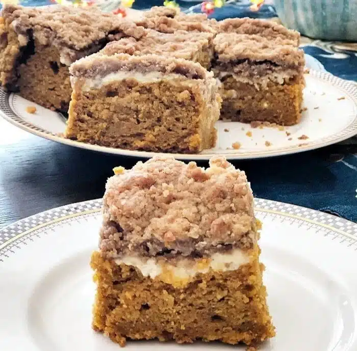 Delicious pumpkin cake with cream cheese frosting and streusel topping served on a plate.